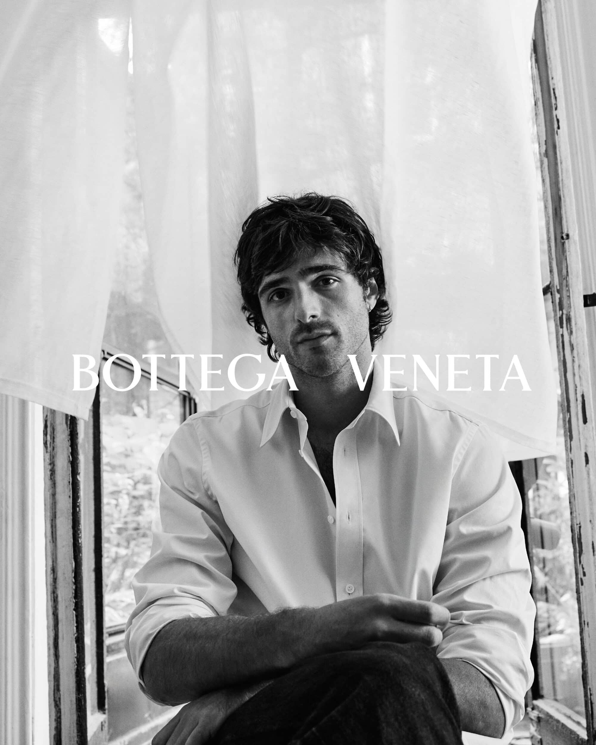 Portrait of a light-skinned adult male with dark hair wearing a white button-down shirt and jeans, sitting in front of a window.