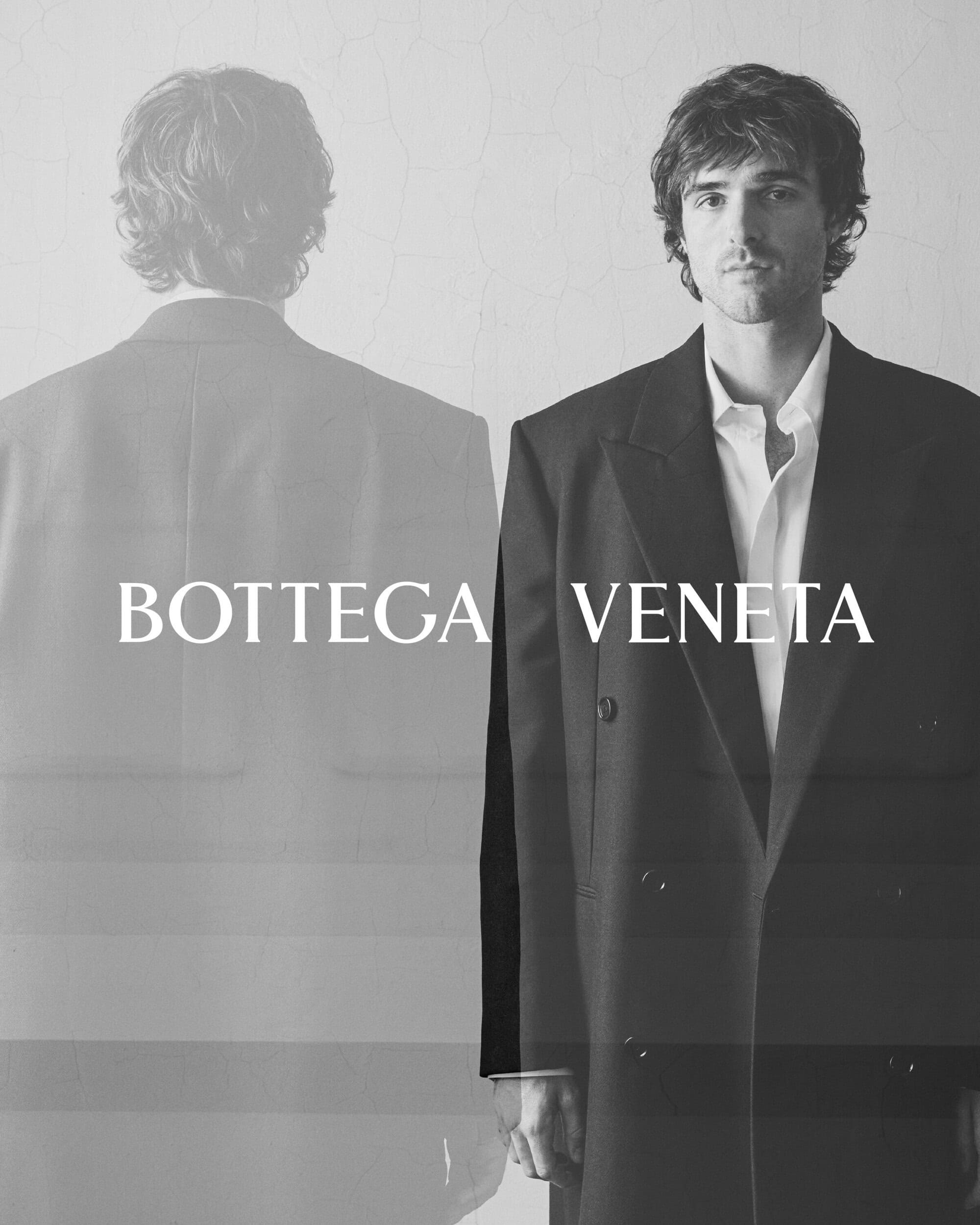 Fashion shot: man in a black overcoat over a white shirt, posing next to a ghosted figure in a black suit and Bottega Veneta logo.