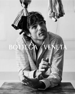 Jacob Elordi wearing a plaid shirt with suspended objects overhead in a black and white campaign portrait.