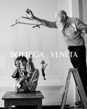 Black and white portrait of Jacob Elordi seated at a table with Duane Michals operating a wooden marionette above him.