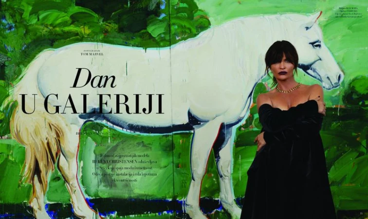 Adult female model poses in black dress against a large, colorful painting of a white horse in a bright, modern art gallery.