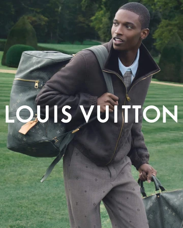 A man carrying two Louis Vuitton monogram travel bags across a green garden lawn during the Spring 2026 campaign.