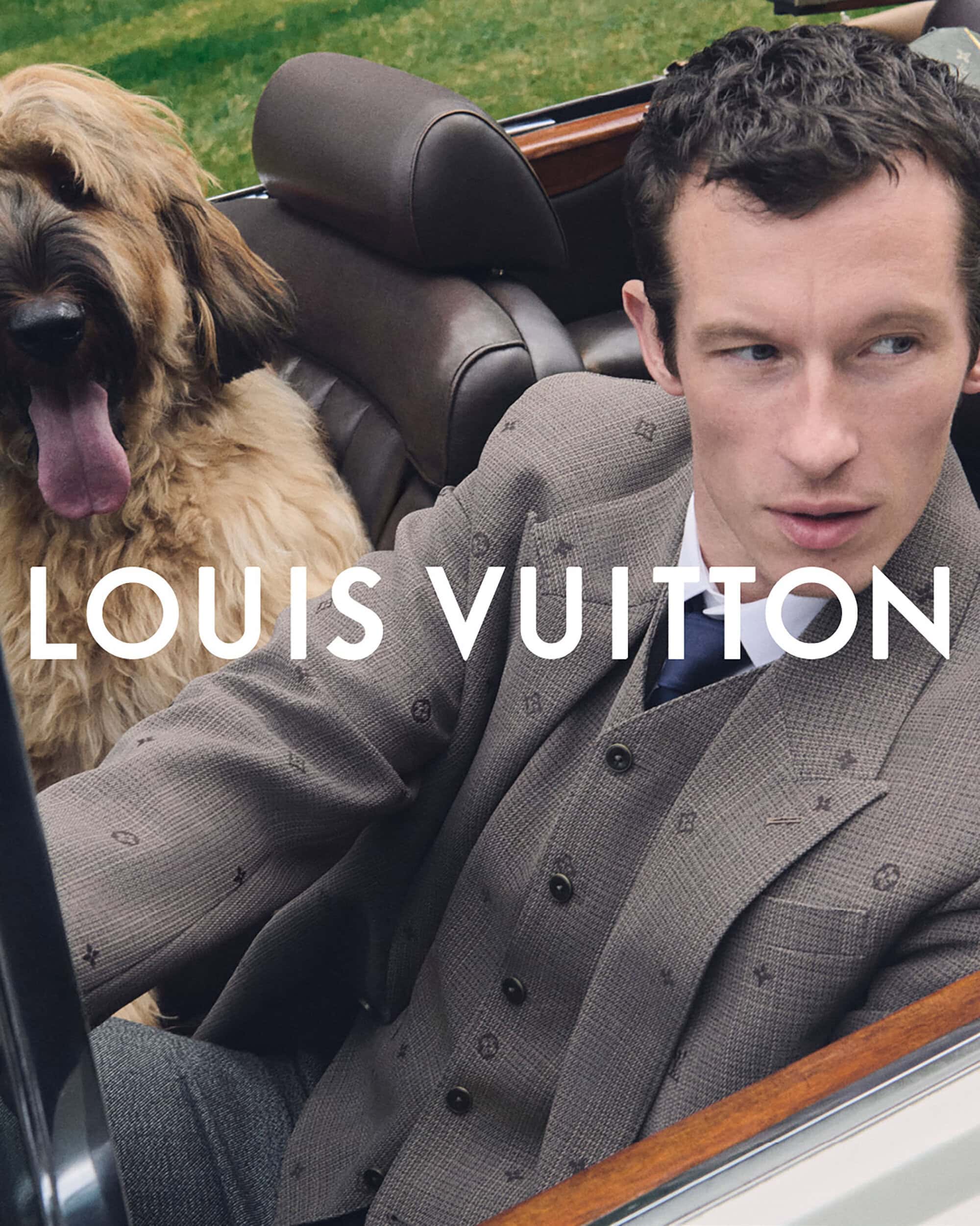 A well-dressed adult male sits in a car with a large dog. The man is wearing a suit and tie, and the dog is panting happily.
