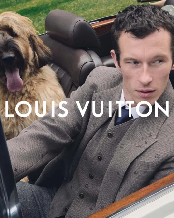 A well-dressed adult male sits in a car with a large dog. The man is wearing a suit and tie, and the dog is panting happily.