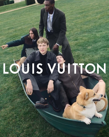 Group of models and a dog posing in a boat on a grassy field for a Louis Vuitton fashion campaign, showcasing menswear and accessories.