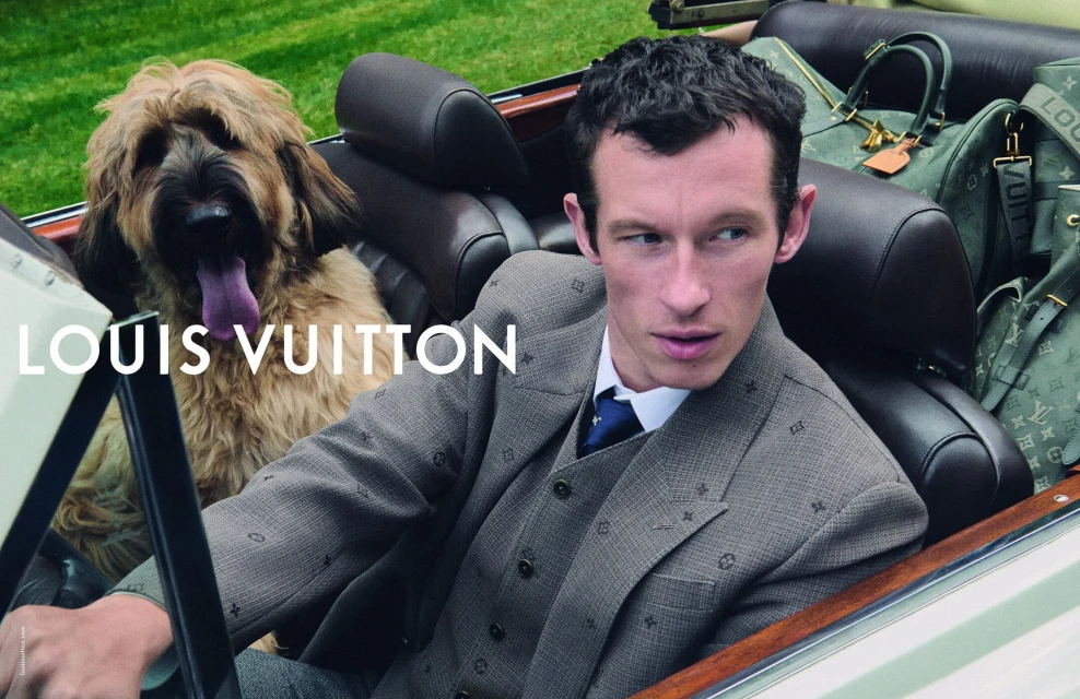 Fashion advertisement featuring a man in a suit with a dog in a car, showcasing Louis Vuitton bags in the background.