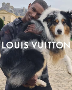 Man holding a large fluffy Australian Shepherd dog against a stone building exterior for Louis Vuitton