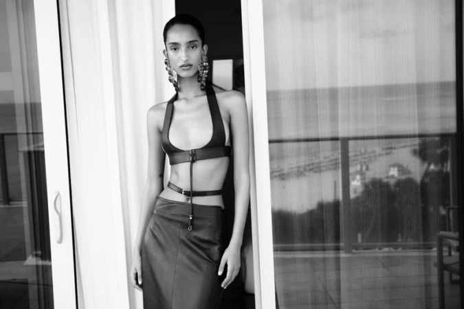Monochrome fashion editorial portrait of a model in a halter top and skirt standing near a balcony door for D Repubblica.