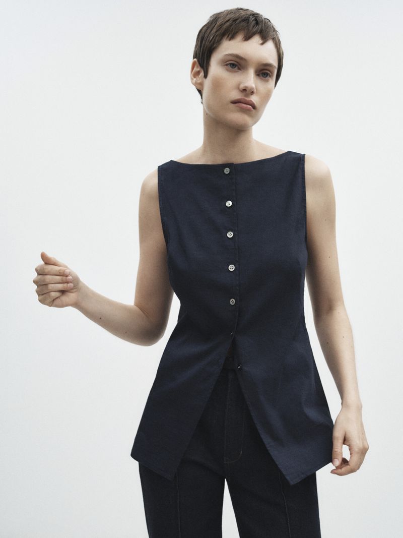 Studio shot of a woman wearing a sleeveless navy top with buttons and matching trousers. The model is posing against a white background.