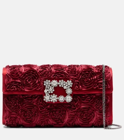 Burgundy satin clutch with rose pattern and crystal buckle, featuring a silver chain strap, against a white background.