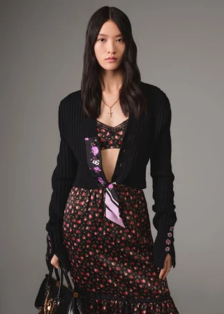 Model in black cardigan and floral print dress holding a handbag against a grey seamless background for Dolce & Gabbana SS26