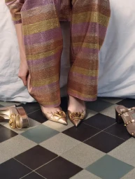 Model seated wearing striped metallic trousers and gold heels with matching shoes on checkered floor