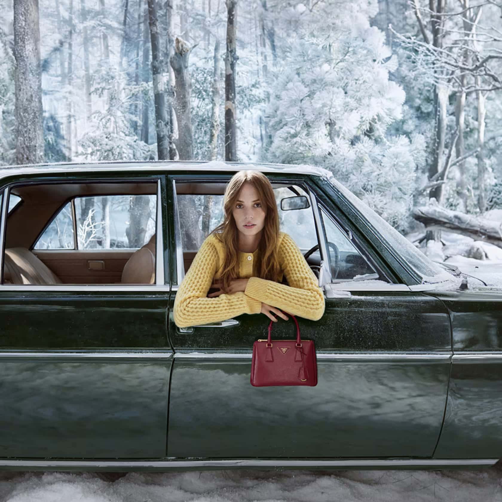 Woman in yellow sweater in car in snow forest holding red Prada handbag. Classic automobile against a background of winter trees.