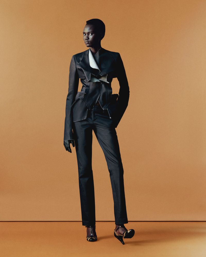 Model Aluel Keror in a structured black tailored suit against a warm solid backdrop
