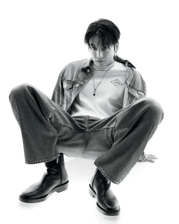 Jung Kook in a denim jacket and wide-leg jeans squatting against a white background for Calvin Klein.