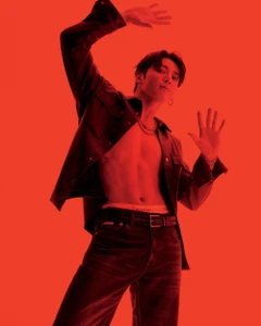 Jung Kook in an open dark shirt and denim jeans posing against a red background for Calvin Klein.