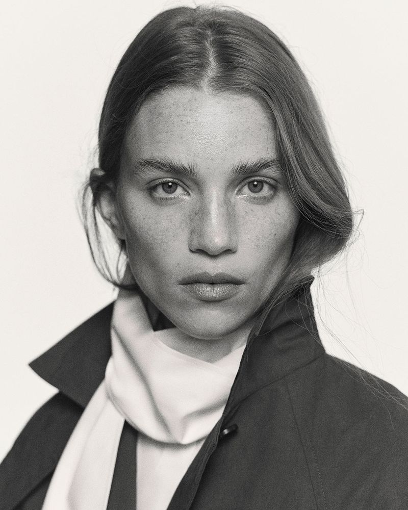 Portrait of Rebecca Leigh Longendyke wearing a dark jacket and white scarf against a plain background