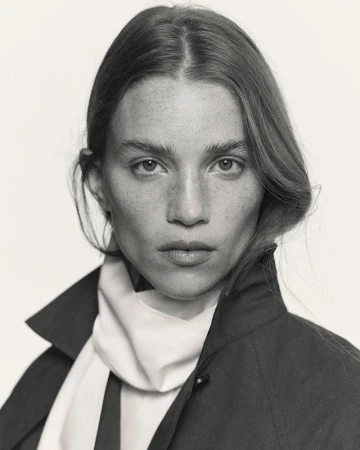 Portrait of Rebecca Leigh Longendyke wearing a dark jacket and white scarf against a plain background
