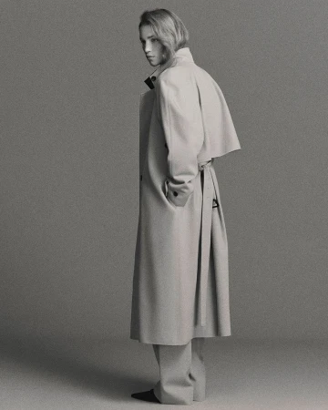 Full-length shot of an adult female with fair skin and blonde hair wearing a neutral trench coat and standing in a photo studio.