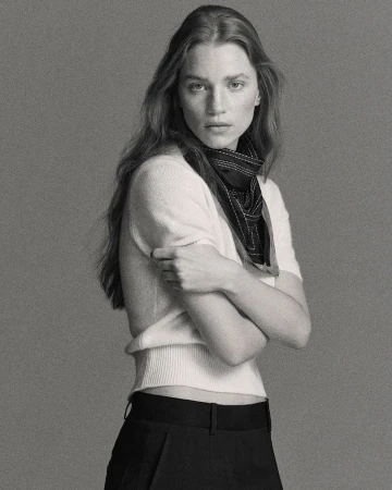 Model Rebecca Leigh Longendyke in a white top and dark scarf against a grey background for COS Spring 2026