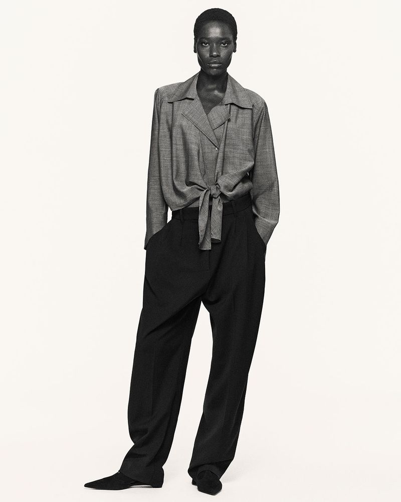 Full-length studio portrait of an African-American woman in a grey blouse and black slacks against a neutral background.