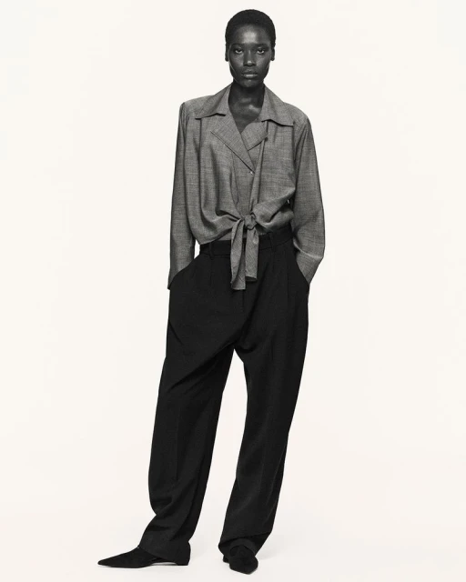 Full-length studio portrait of an African-American woman in a grey blouse and black slacks against a neutral background.