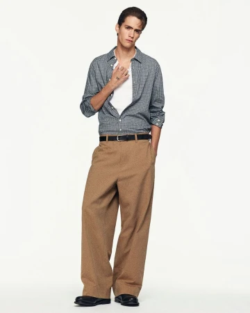 Male model in a plaid button-down shirt and brown trousers against a plain white background for COS Spring 2026 lookbook