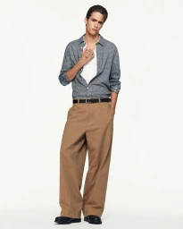 Male model in a plaid button-down shirt and brown trousers against a plain white background for COS Spring 2026 lookbook
