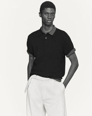 Model in a black polo shirt and white trousers against a neutral background for COS Spring 2026