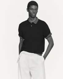 Model in a black polo shirt and white trousers against a neutral background for COS Spring 2026