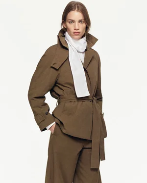 Model wearing a structured brown belted jacket and white scarf against a plain white studio background.