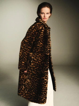 Model wearing a leopard print faux fur coat over white trousers against a neutral grey studio backdrop