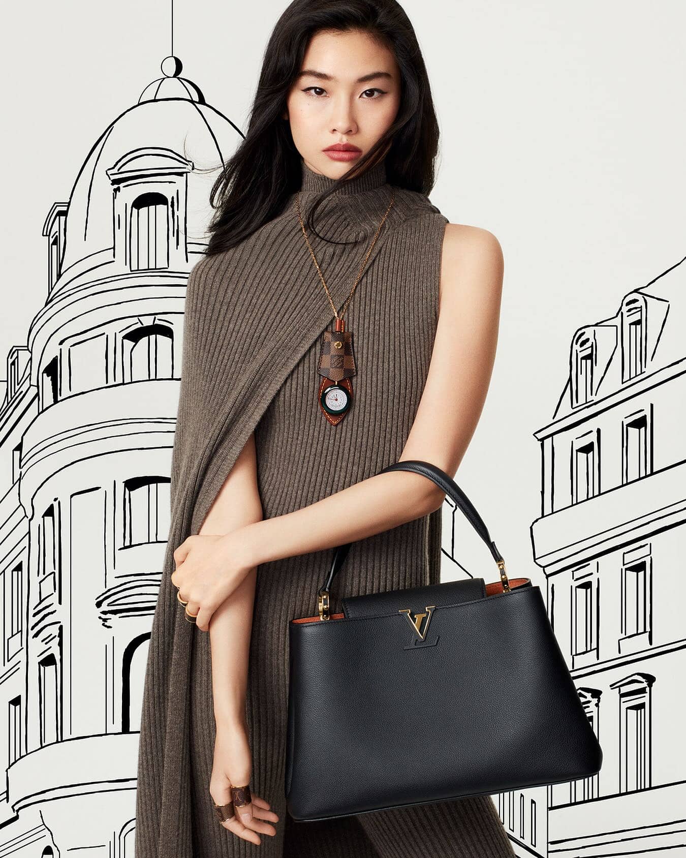 Asian woman models a black leather handbag with gold logo in a fashion shot against a stylized cityscape backdrop.