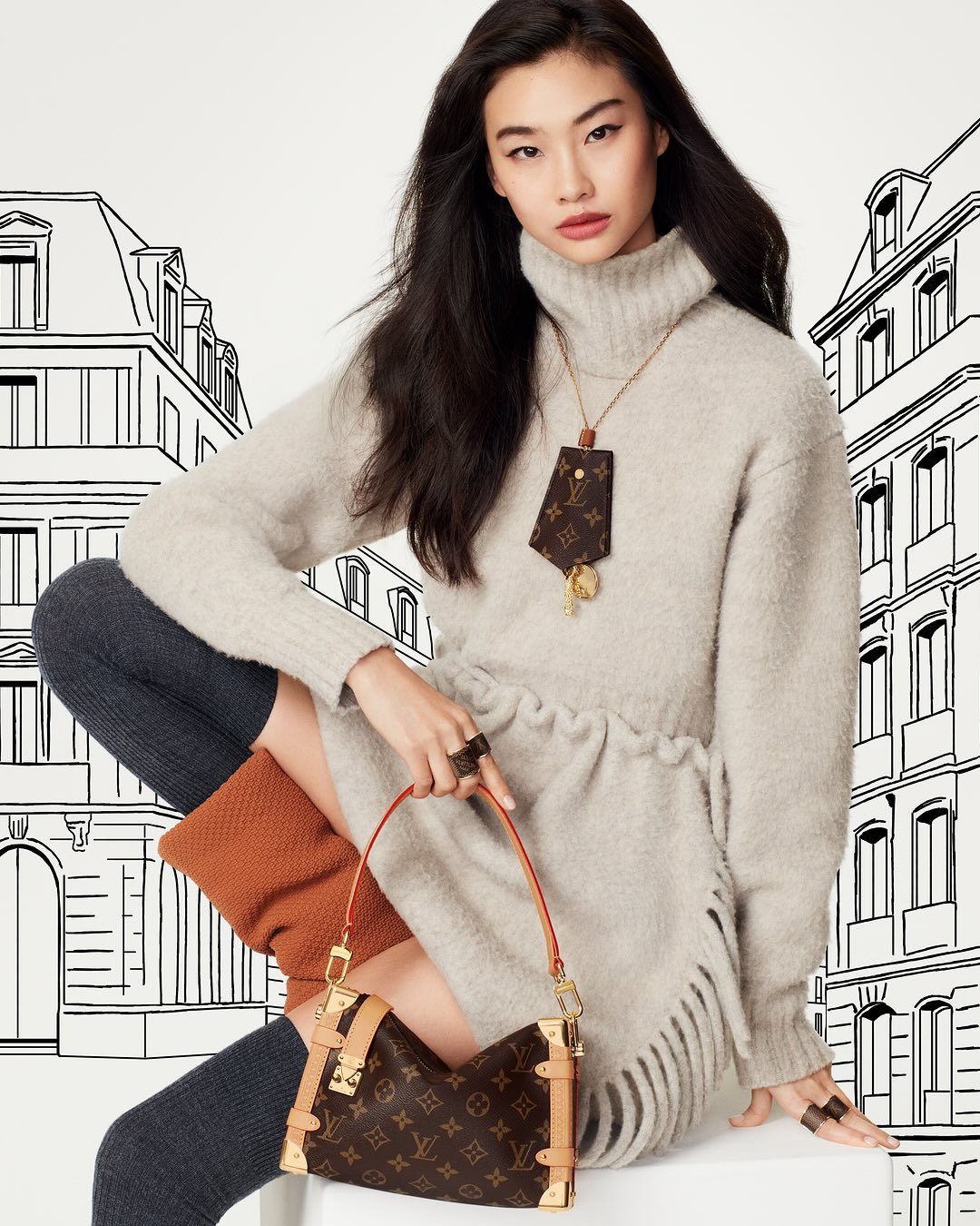 Elegant Asian woman poses indoors wearing a beige sweater dress, brown handbag, and accessories, against a white backdrop with building illustrations.
