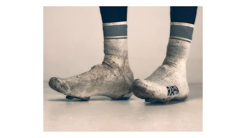 Close-up of dirty white cycling shoe covers and socks with a blue stripe, showing wear and tear from an outdoor bike ride.