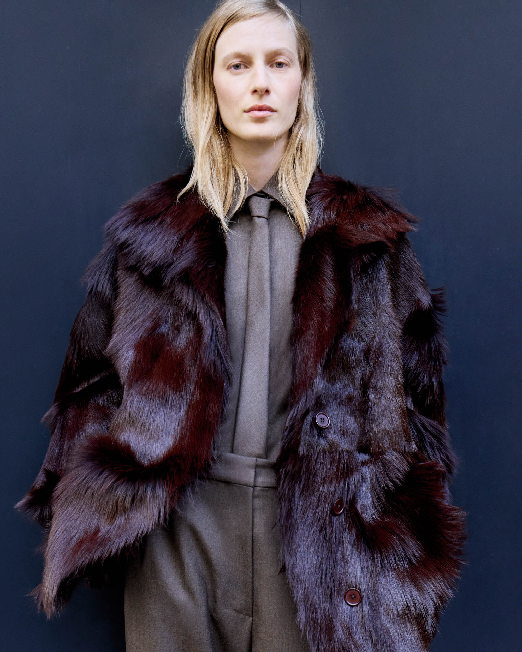 Portrait of a woman wearing a fur coat and tie, set against a dark background, emphasizing fashion and classic style.