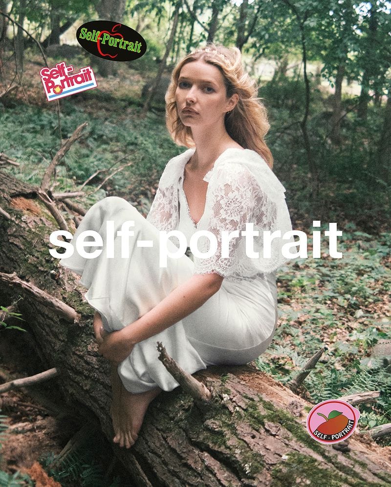 Blonde woman in a white dress sitting on a fallen tree in the forest. 'Self Portrait' text overlay. Beauty and fashion photography.