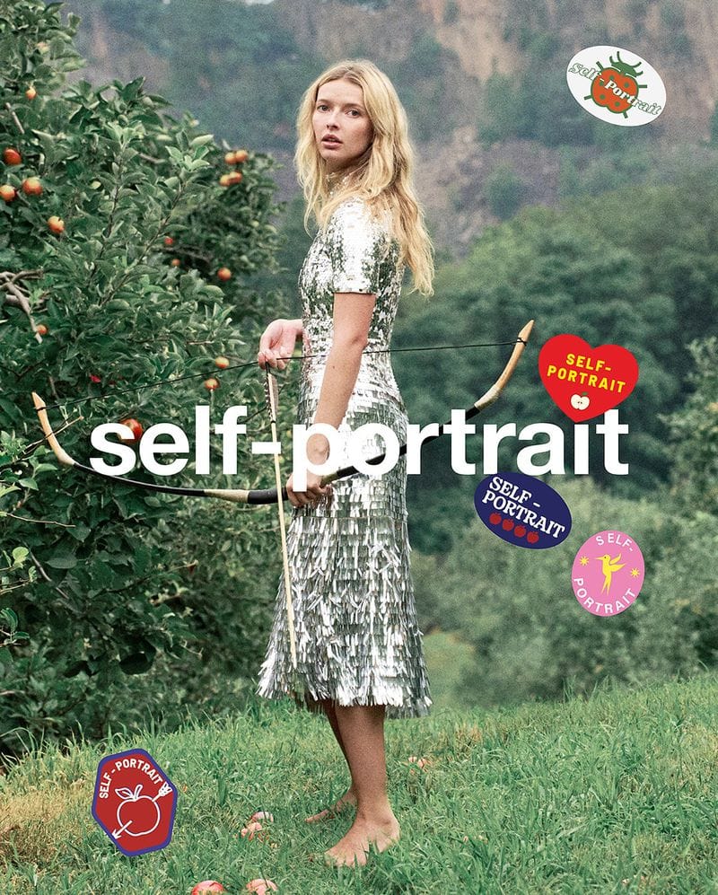 Woman in shimmering dress holding bow and arrow, standing barefoot in a field near fruit trees and 'self-portrait' graphic stickers.