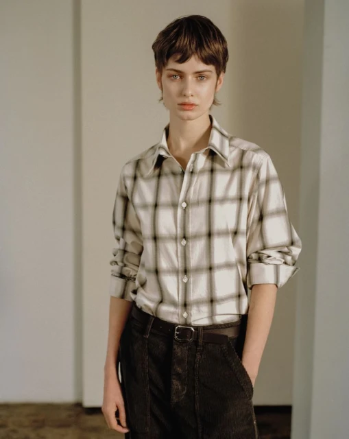 Indoor portrait of a young adult woman with short brown hair. She is wearing a plaid button-down shirt and corduroy pants.