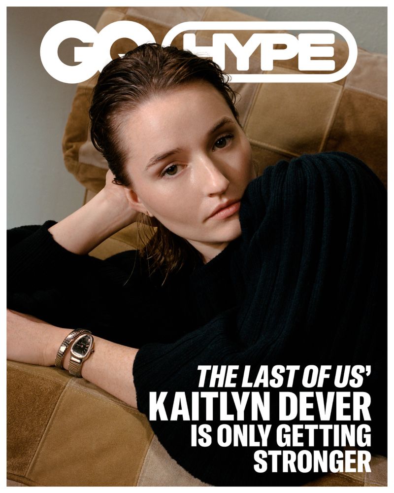 Kaitlyn Dever on a magazine cover, wearing a black sweater, metal watch, posing against a patchwork leather chair, indoor.