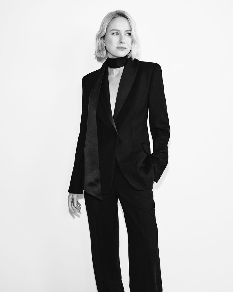 Black and white portrait of an adult woman in a black suit and scarf, against a bright white background in a studio setting.