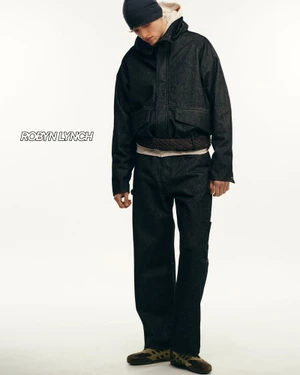 Model wearing dark denim jacket and matching trousers with a beanie against a white seamless background