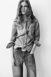 Black and white portrait of a female model wearing a denim shirt and jeans against a white seamless background