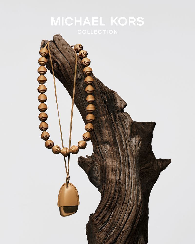 Michael Kors Collection necklace on a piece of driftwood against a light background in a product shot promoting jewelry.