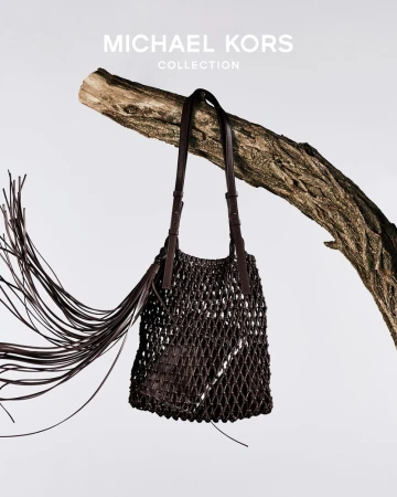 Dark brown leather woven shoulder bag hanging from a gnarled tree branch against a pale background