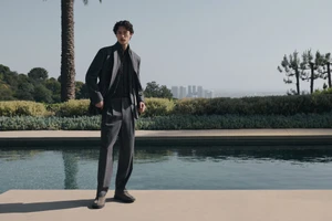 Man wearing a grey suit standing by an outdoor swimming pool with a distant city skyline in the background for Neiman Marcus