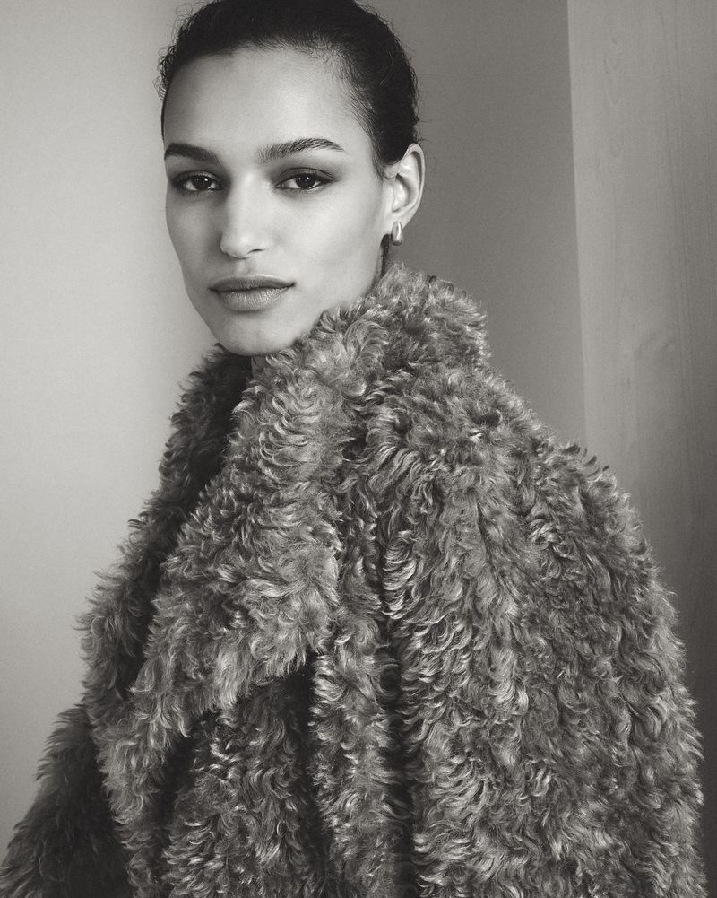 Monochrome portrait of a woman in a textured fur coat, looking at the camera against a neutral background in a close-up studio shot.