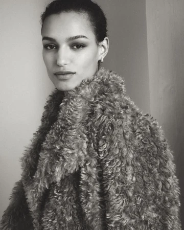Monochrome portrait of a woman in a textured fur coat, looking at the camera against a neutral background in a close-up studio shot.