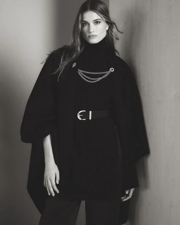 Model in black turtleneck and draped outerwear posing against a neutral wall for Donna Karan lookbook.