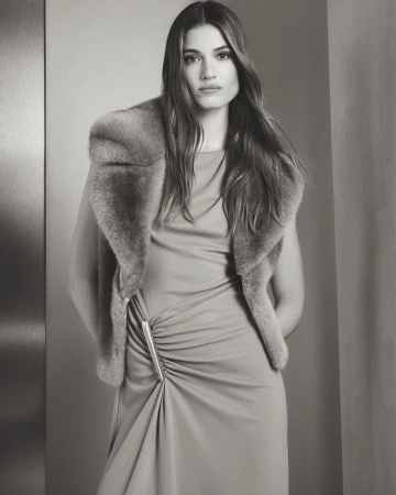 Portrait of a woman wearing a dress and fur stole, posing indoors in a neutral-toned setting with natural light. Fashion advertisement.